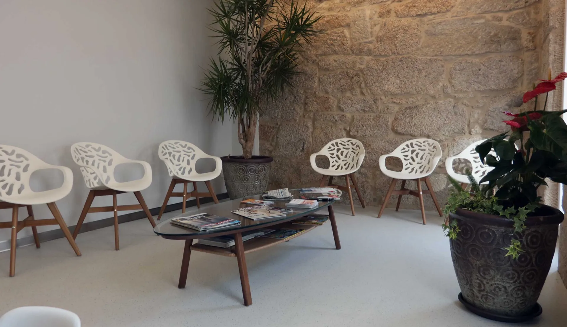 Sala de espera de la Clínica Dental Ocampo Alfaya con el muro de piedra original y sillas blancas