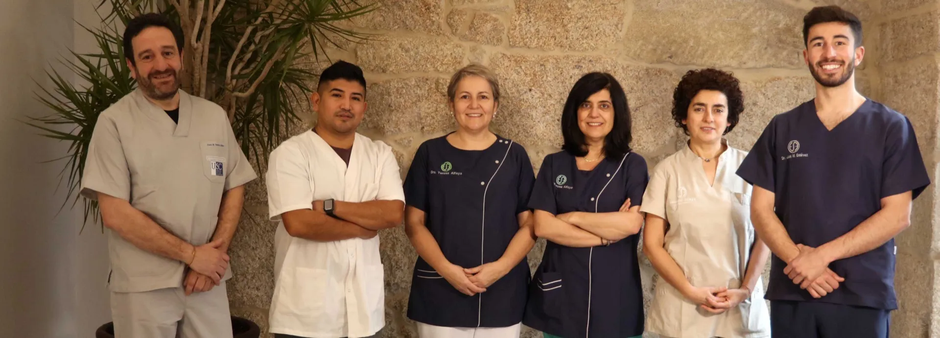 Equipo de la Clínica Dental Ocampo Alfaya en fila ante el muro de piedra de la clínica en Redondela