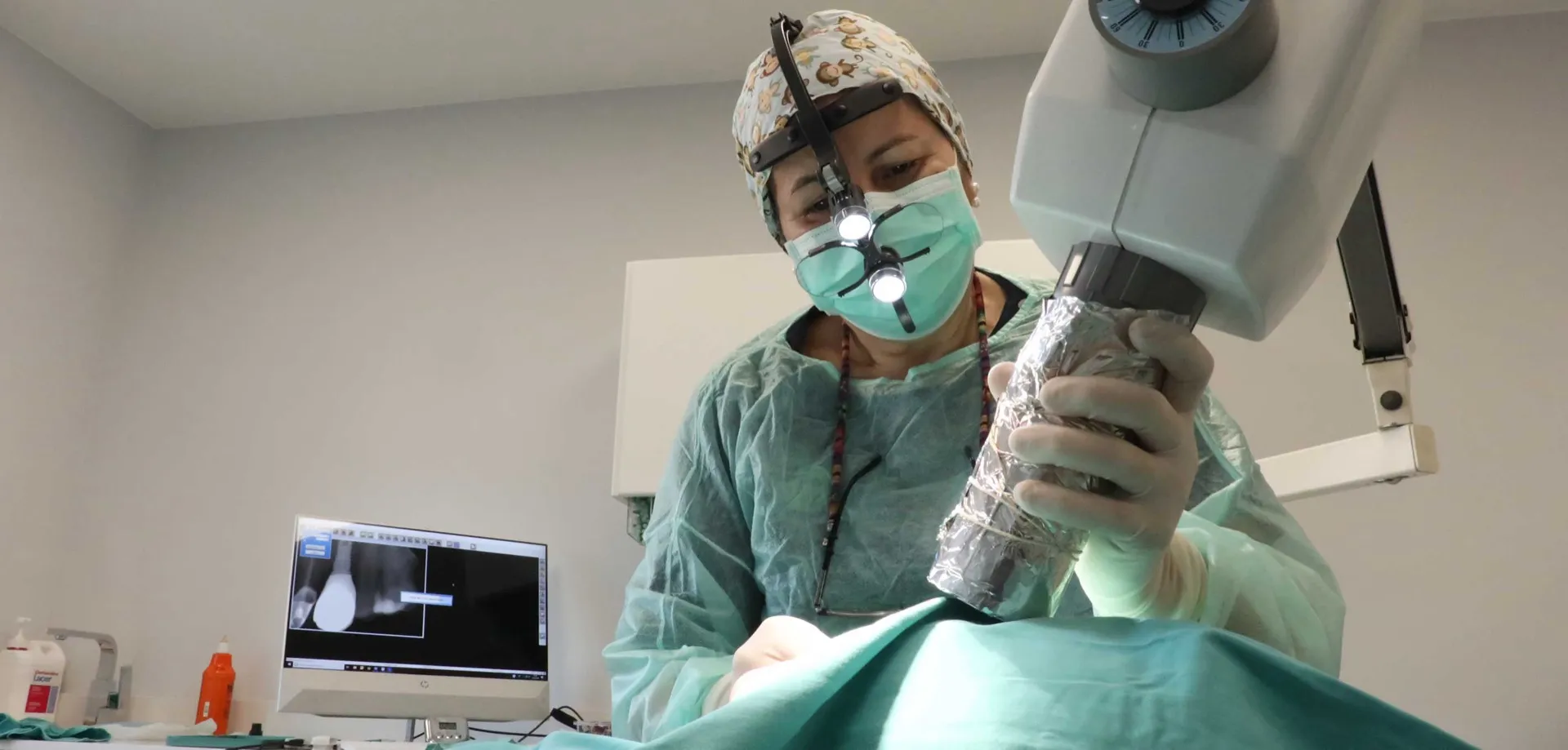 Doctora de la Clínica Dental Ocampo Alfaya ajustando el microscopio durante una cirugía, con la radiografía en pantalla